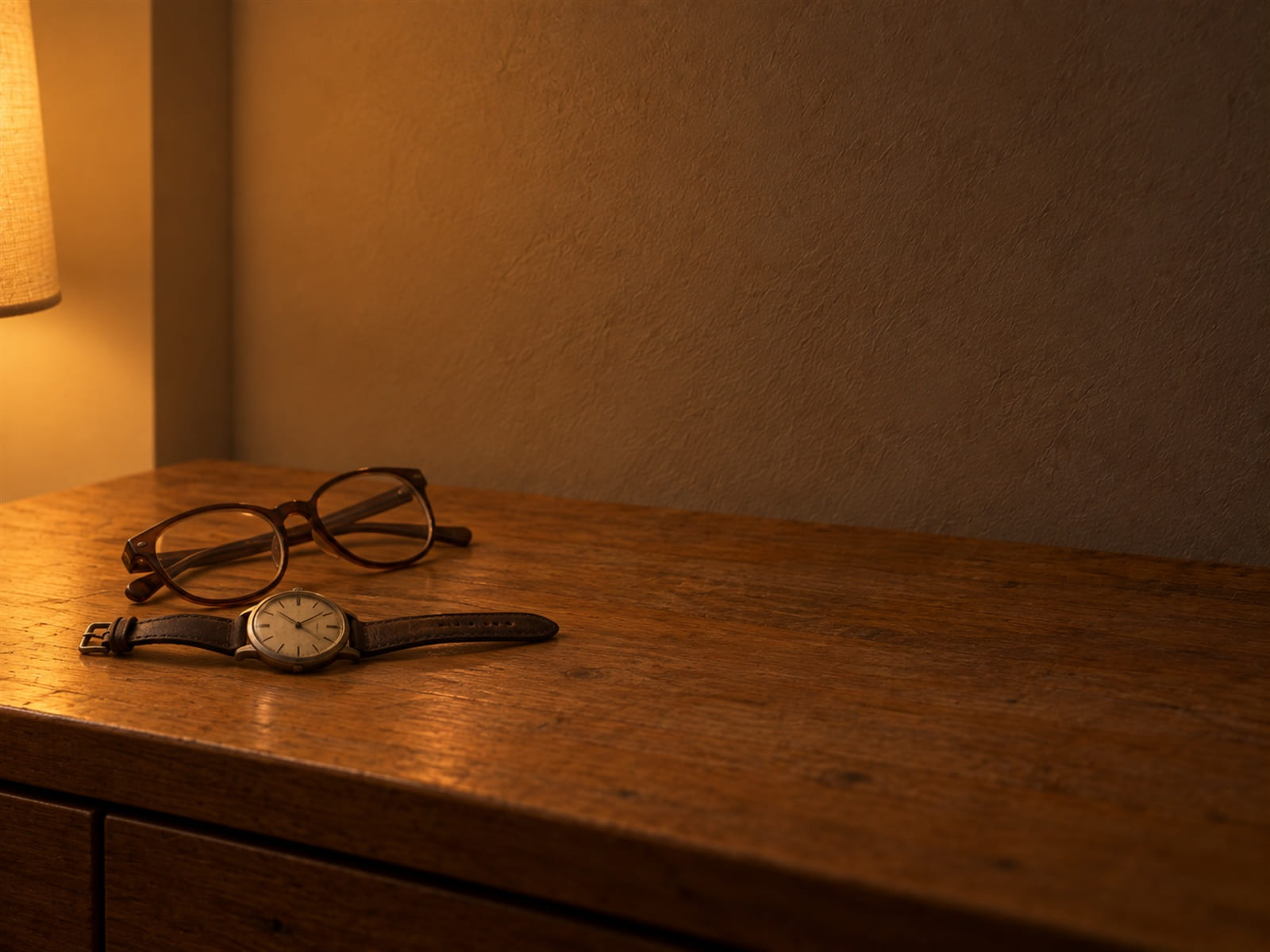 Un reloj de pulsera antiguo y unas gafas de lectura sobre una cómoda de madera