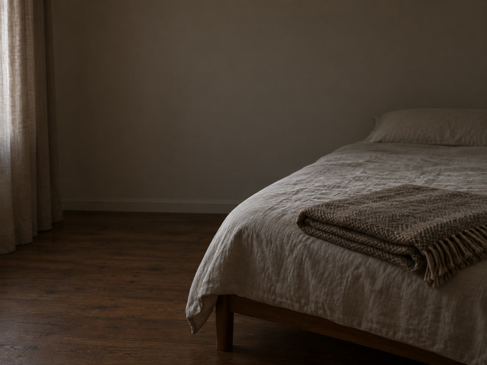 A folded blanket at the foot of a bed in gray early light