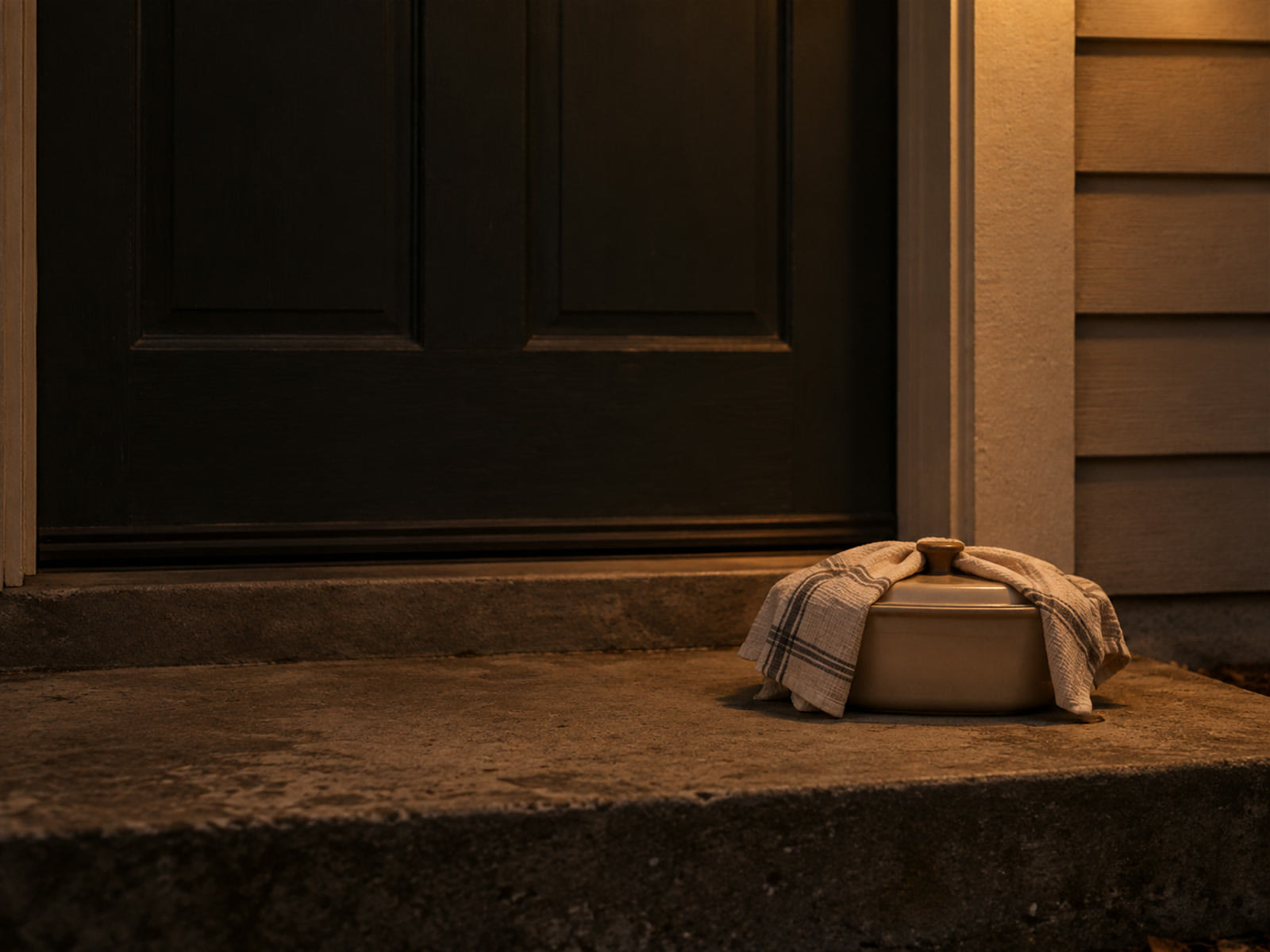 A covered casserole dish wrapped in a tea towel, set down on a front doorstep