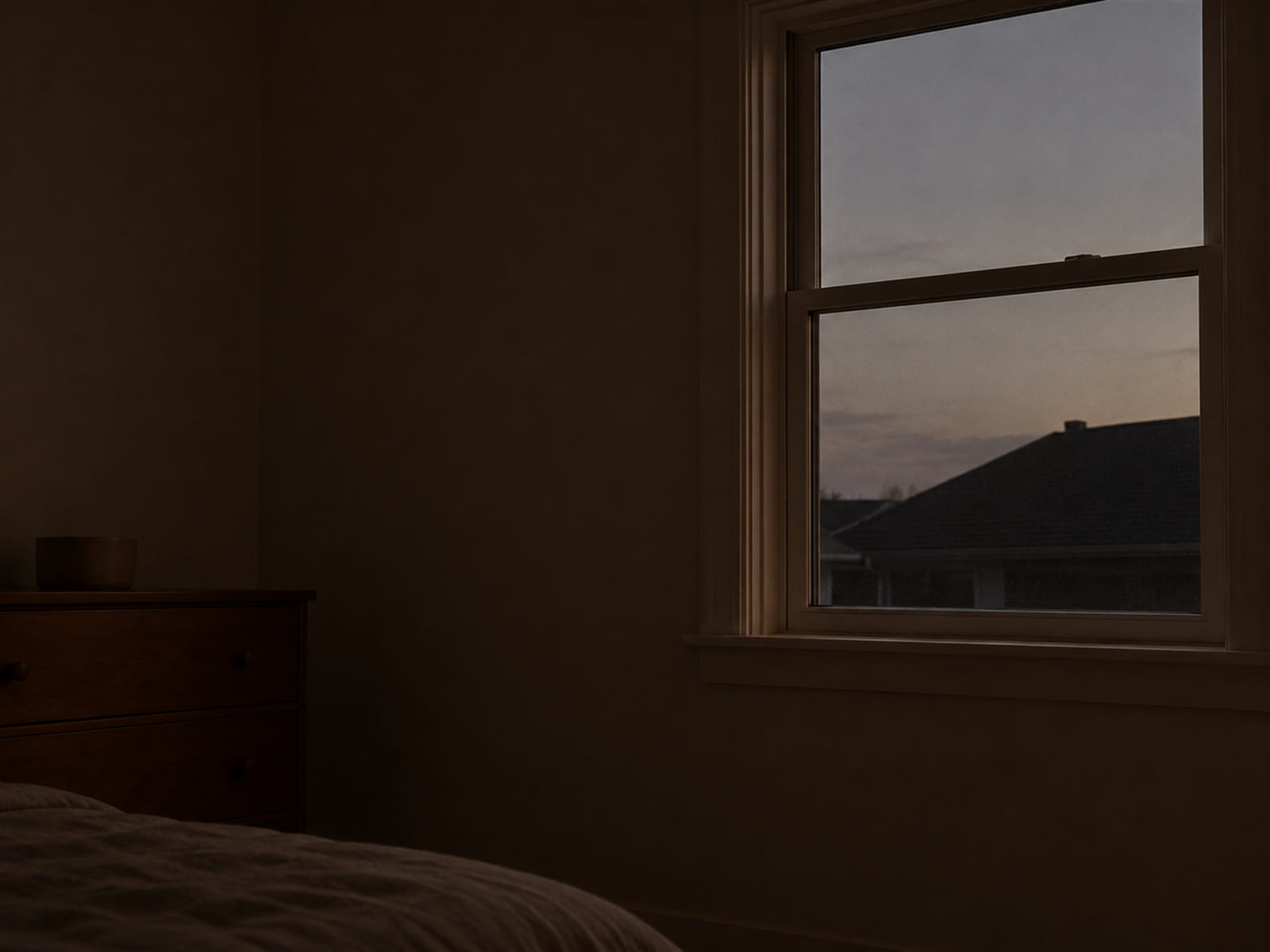 A window before dawn, the sky just beginning to separate from the roofline