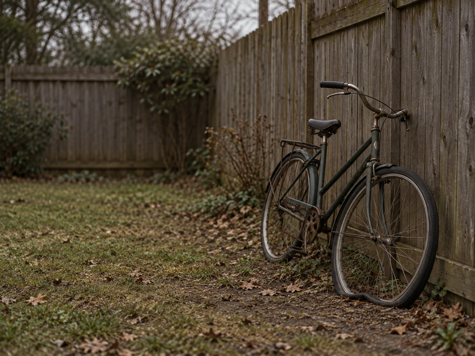 A bicycle with a flat tire leaning against a wooden fence on an overcast afternoon