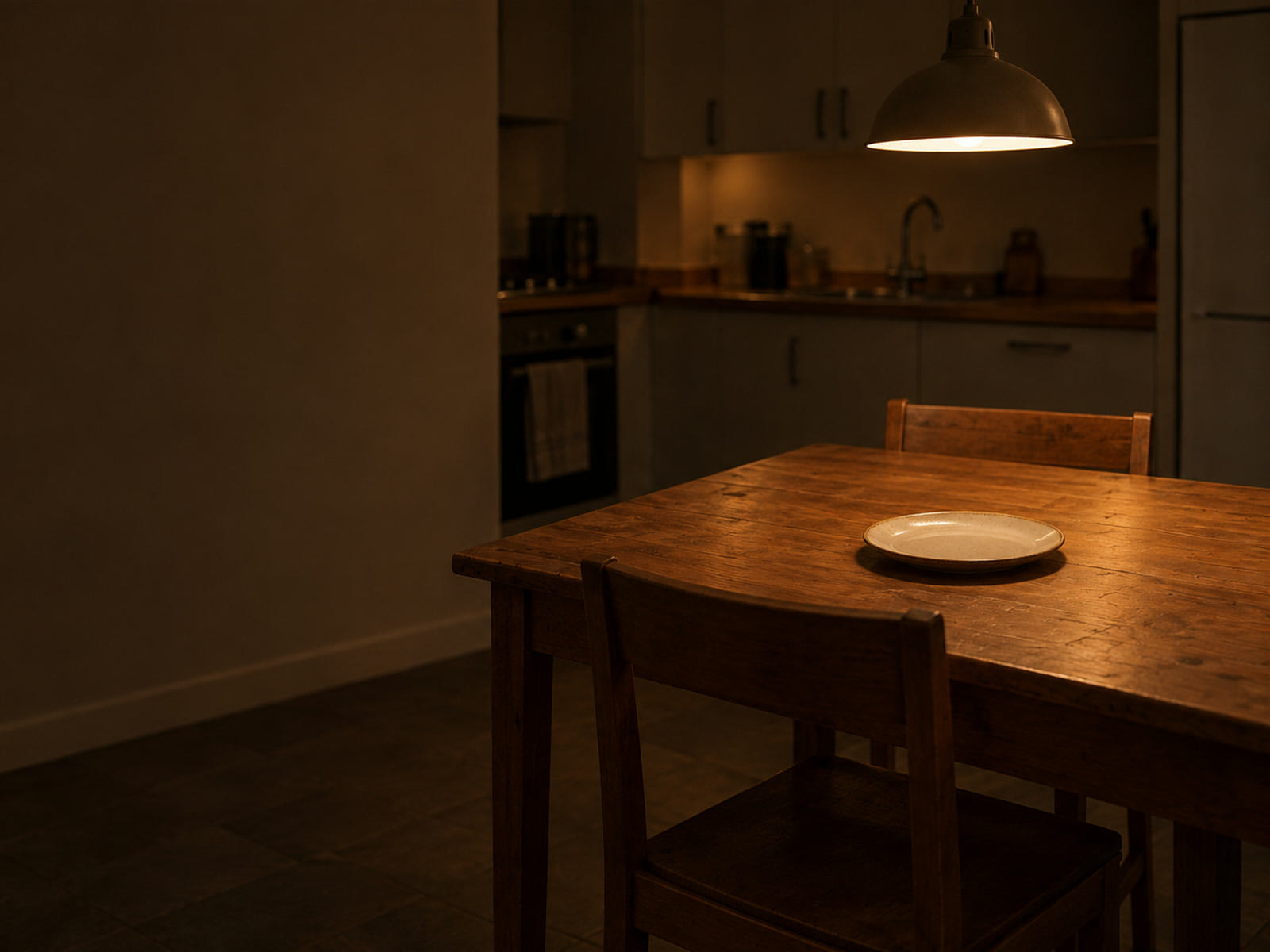 A small kitchen table laid with one plate, the second chair pushed in, under a hanging lamp