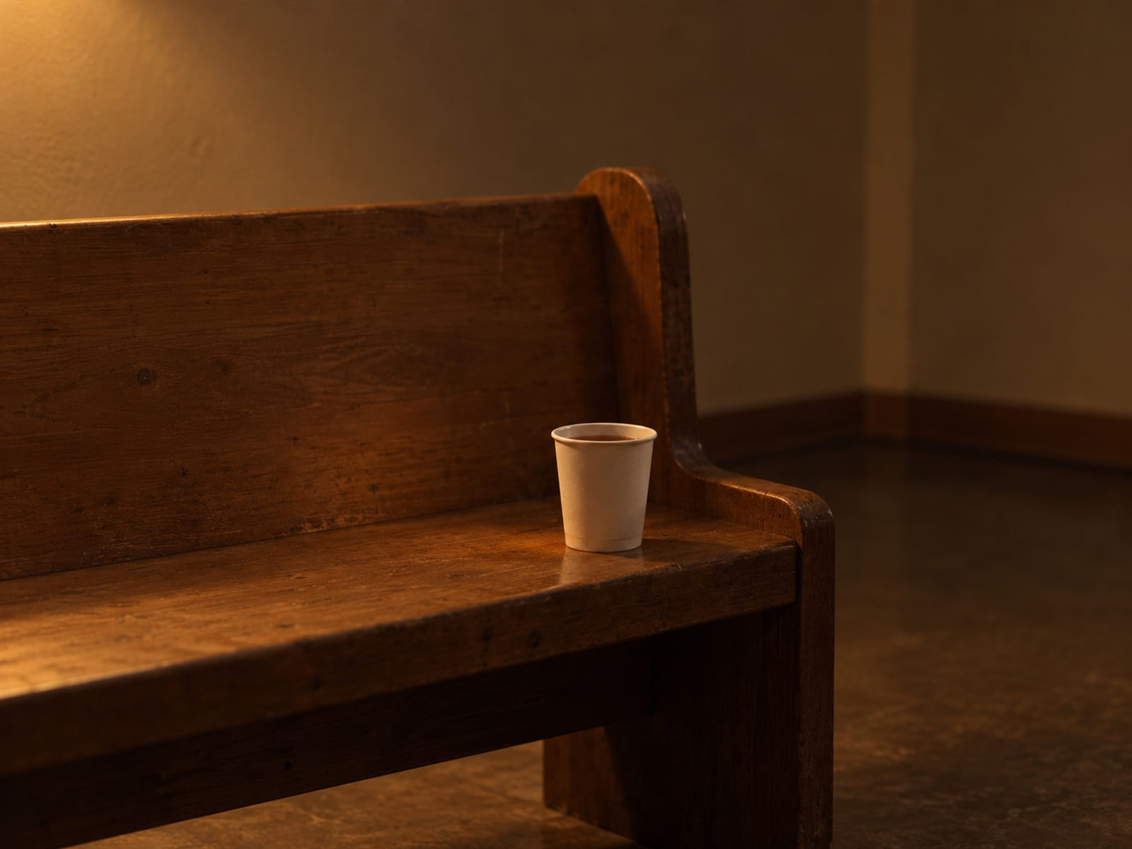 A paper cup of tea on the end of a wooden pew