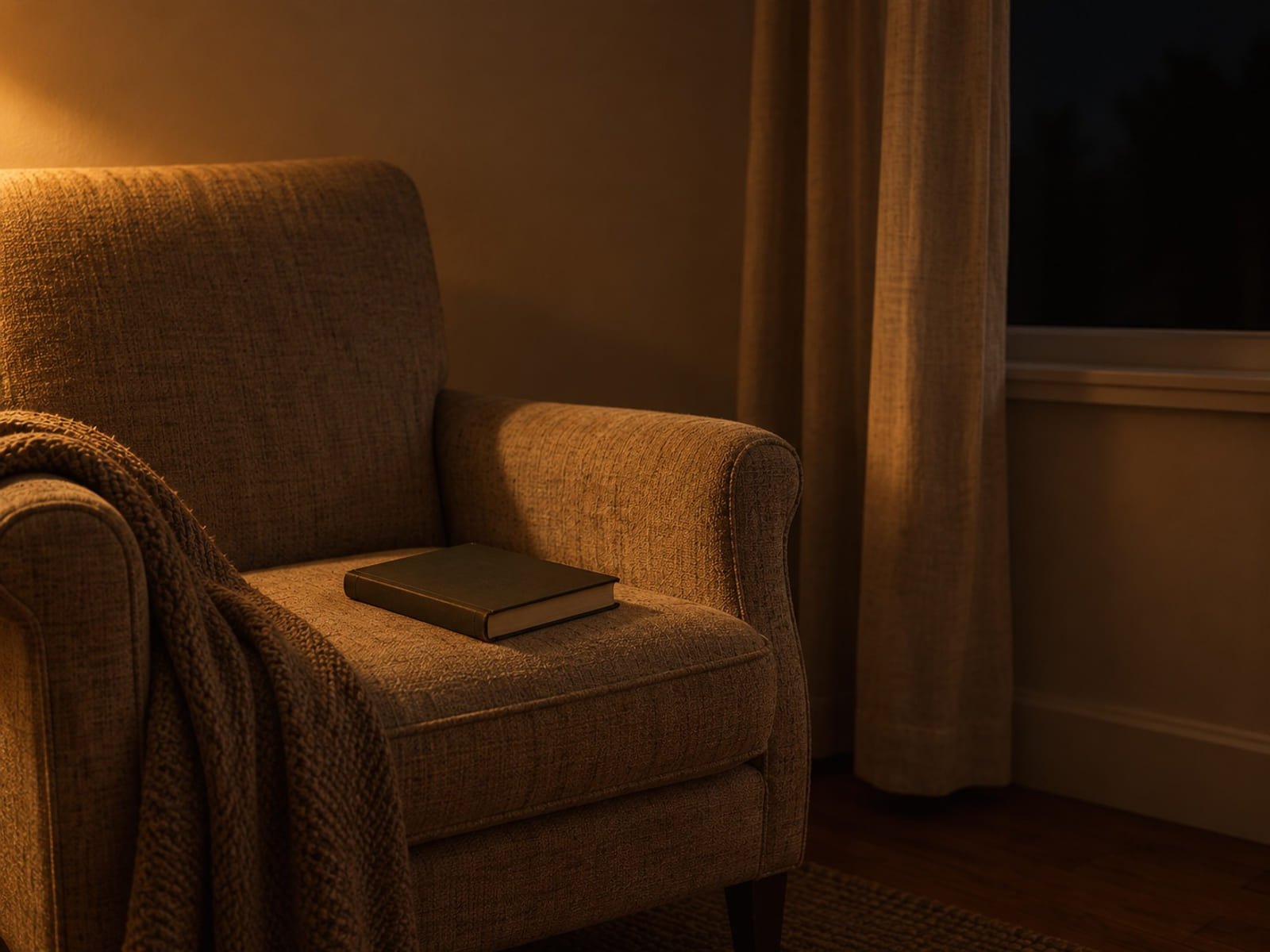 An armchair by a window with a closed book lying face down on the seat