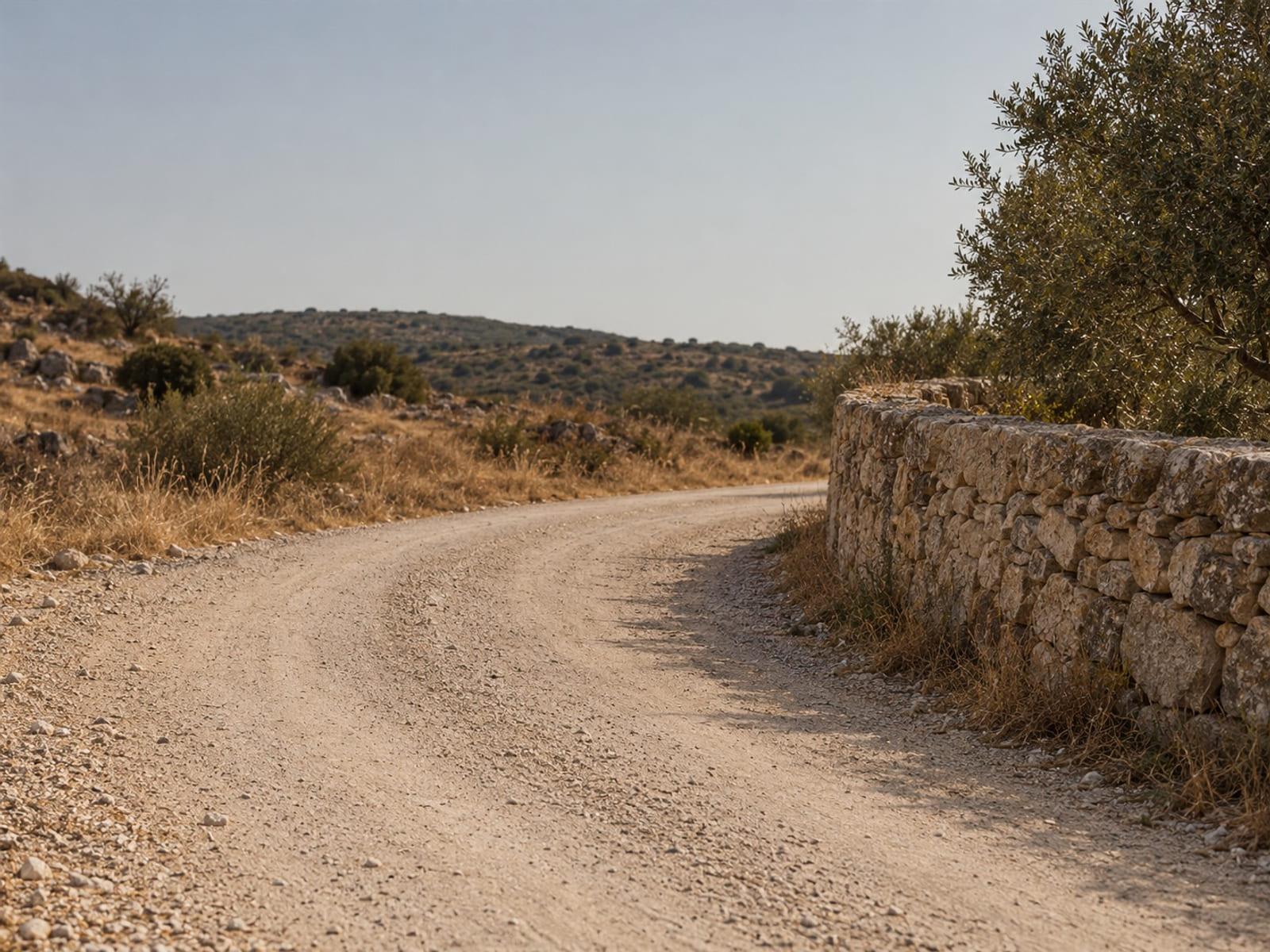 A dusty stone road bending toward a low wall under a clear sky