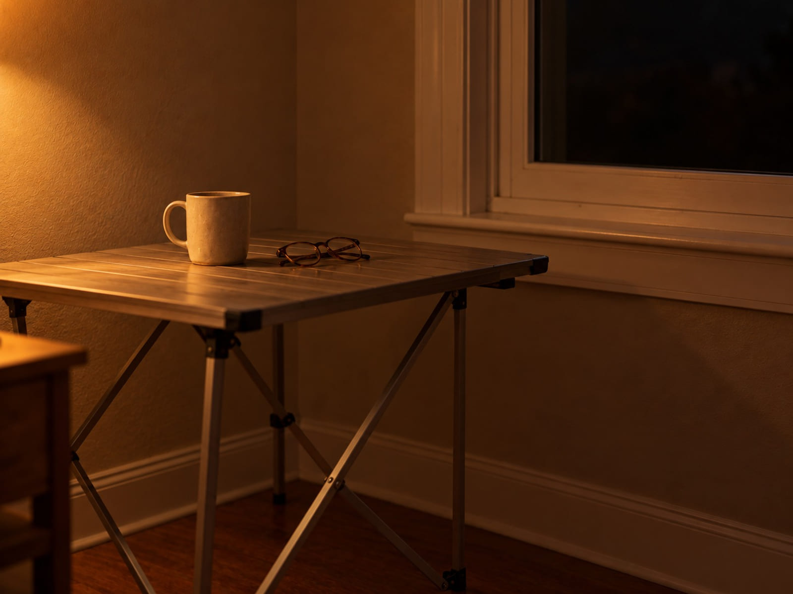 A single mug and a pair of reading glasses on a camper table by a small window